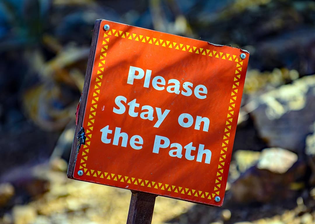 תצלום כללי של שלט כתום על עמוד ובו הכיתוב Please Stay on the Path בשטח פתוח