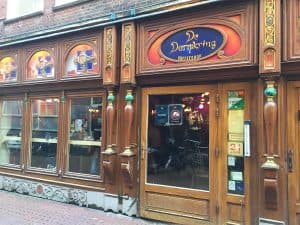 שלט הזכוכית הצבעוני של De Dampkring Coffeeshop מעל חלונות העץ המגולפים ברחוב