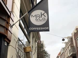 שלט התלייה של מיסטר קיי עם הלוגו MR K & Co. בולט מעל הרחוב בצילום מלמטה
