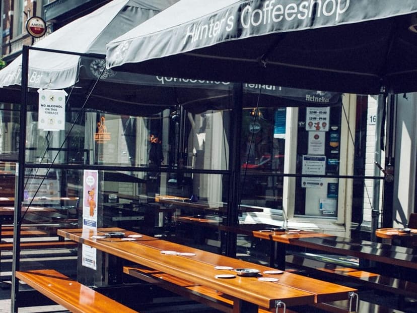 סוכך ובו הכיתוב Hunter's Coffeeshop מעל מרפסת ריקה עם ספסלי עץ ארוכים ומאפרות